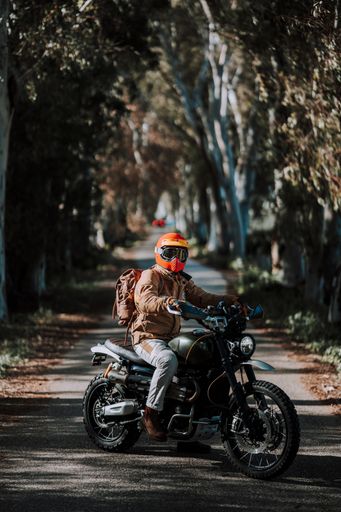Man on motorcycle with backpack and helmet riding through forest on road