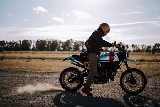 Man in dark jacket riding a motorcycle, kicking up dust with tire