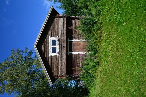 A vertical shot of a Northern Swedish barn with green grasses under a clear blue sky