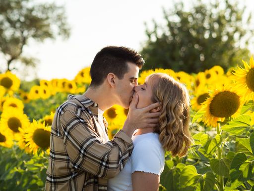 A portrait of a young cute couple kissing in a sunflower field