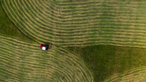 An aerial shot of a tractor on green farmland during daylight