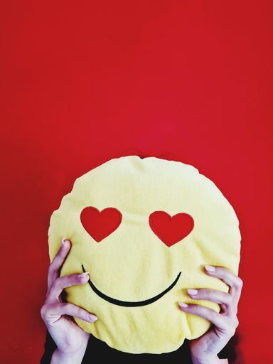 A woman holding a pillow in the form of a smiling face in front of her face