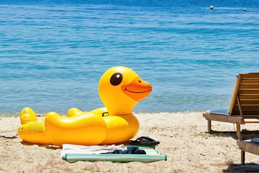 A yellow inflatable duck sitting on the beach in front of the sea.