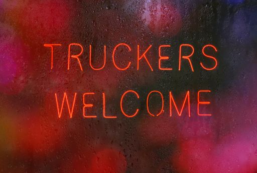 A vintage neon Truckers Welcome sign on a wet window