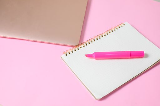 A top view of a marker on an open notebook beside a laptop isolated on a pink surface with copyspace