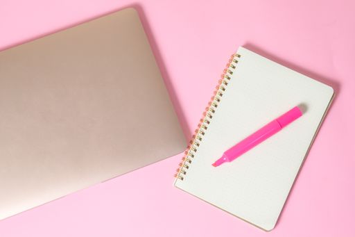 A top view of a marker on an open notebook beside a laptop isolated on a pink surface with copyspace
