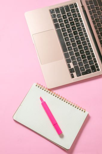 A top view of a marker on an open notebook beside a laptop isolated on a pink surface with copyspace
