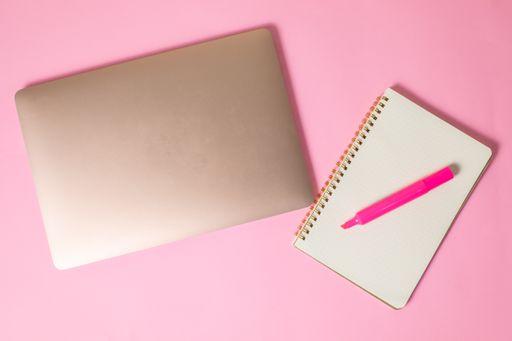 A top view of a marker on an open notebook beside a laptop isolated on a pink surface with copyspace