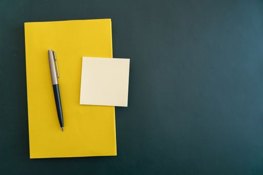 a Yellow book with pen and sticky notes on dark green flat background.
