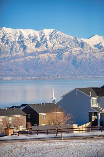 A vertical shot of countryside landscape with houses on the bay of a lake and snowy hills