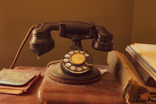 A high angle shot of a dusty retro model of telephone with old books and cards