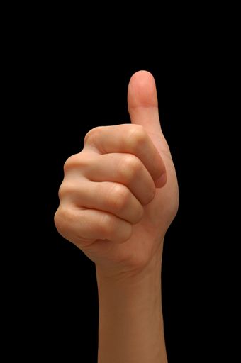 A closeup of a thumbs up hand signal isolated on a black background with free space for text