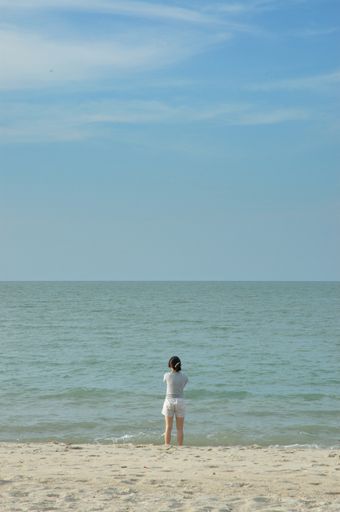 A vertical shot of a female standing on a sandy beach