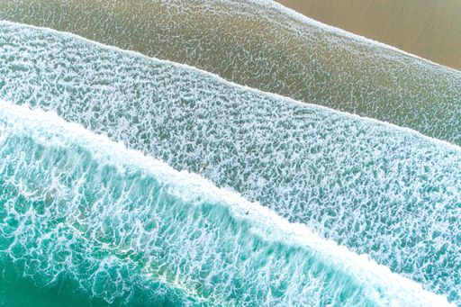 An aerial view of beautiful foamy waves on a sandy shore