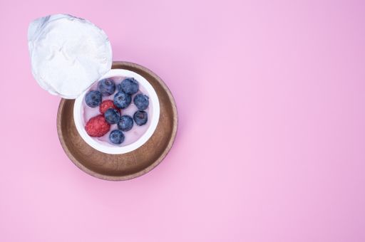 A top view of a berry yogurt in a plastic cup on a pink background