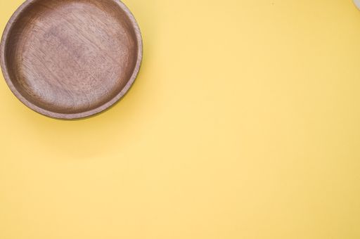 A top view of a wooden round tray on a yellow background