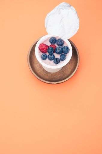 A berry yogurt in a plastic cup on an orange background