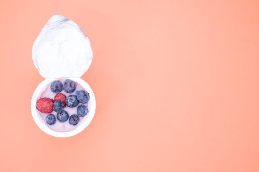 A berry yogurt in a plastic cup on an orange background