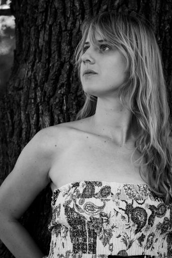 A Grayscale photo of a blonde girl leaning against a tree