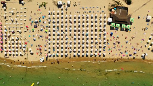 An aerial overhead shot of a highly populated beach with parasols and a wooden cafe on the side