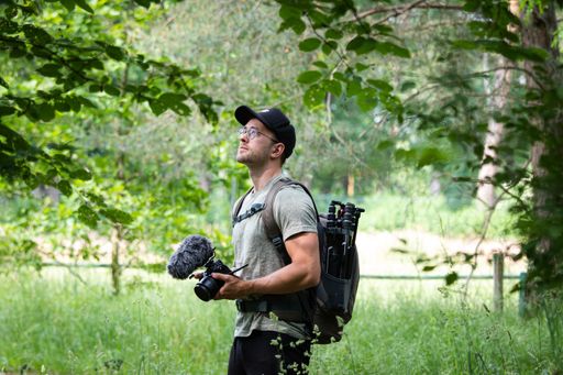 A cool Caucasian man photographer holding camera with backpack outdoors