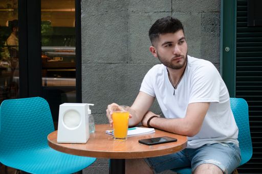A young East Asian man sitting at an outdoor cafe and drinking orange juice