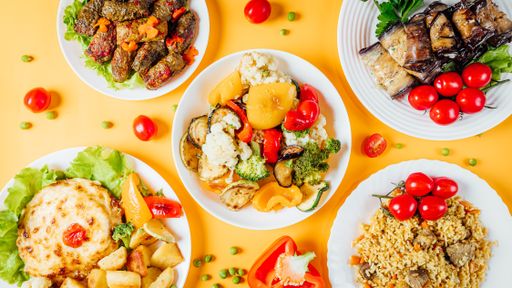 A top view of a white plate filled with Lebanese food with meat, rice, cheesy dish, and colorful vegetables over an orange background