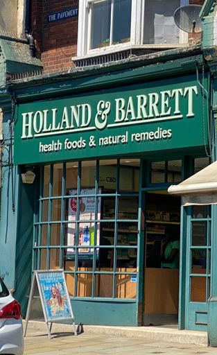 Angled view of front facade of branch of health food retailer Holland & Barrett in High Street, Reigate, Surrey, England, United Kingdom, on sunny day