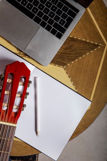 A vertical shot of a Spanish guitar next to a laptop with online guitar lessons of choice