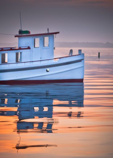 A vertical closeup shot of a small white boat with red lines in a calm sea at sunset