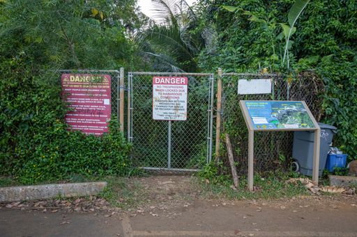 A locked fence and trail closure signs warn visitors to Queen's Bath, a popular yet dangerous natural attraction on Kauai's north shore.