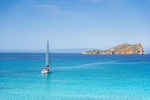 Sailboat sailing on crystal turquoise waters in the mediterranean sea with an island in the background
