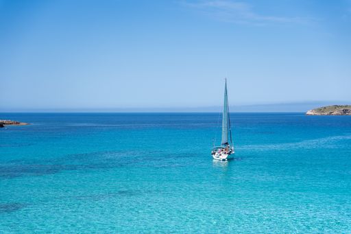 Sailboat sailing on crystal turquoise waters in the mediterranean sea with an island in the background