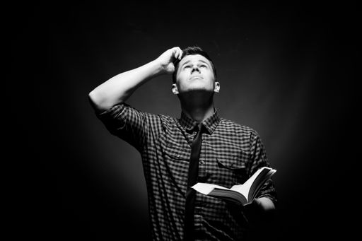A well dressed man holding a Bible and looking up at God in confusion in grayscale