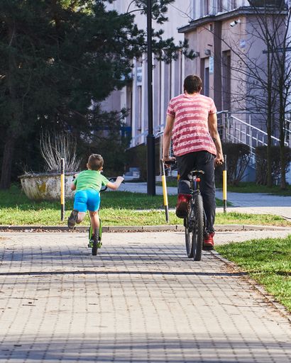 A rear view of a man and a boy riding a bicycle and scooter in a park
