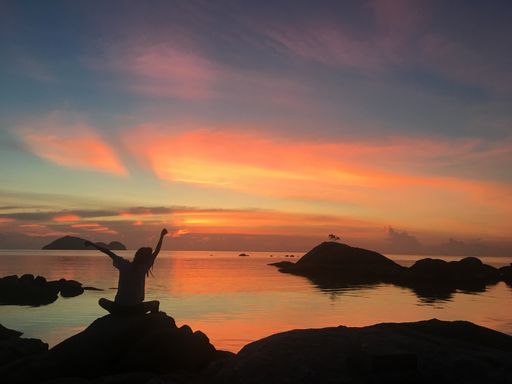 A person posing on a cliff by the sea on a sunset sky background, Phangan island, Thailand