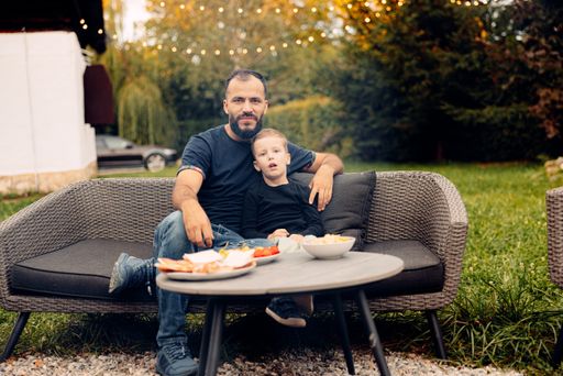 A man sitting on a black couch with his son in the backyard