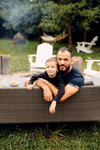 A man sitting on a black couch with his son in the backyard