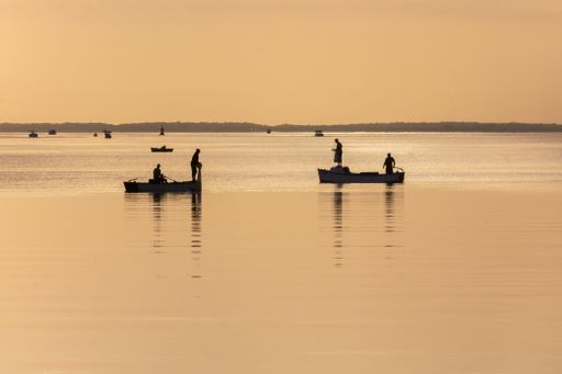 A beautiful sunset at sea with silhouettes of people on small boats under a clear sky