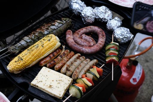 A high angle shot of seasoned vegetables on skewers, sausages, cheese and stuffed fish on a grill