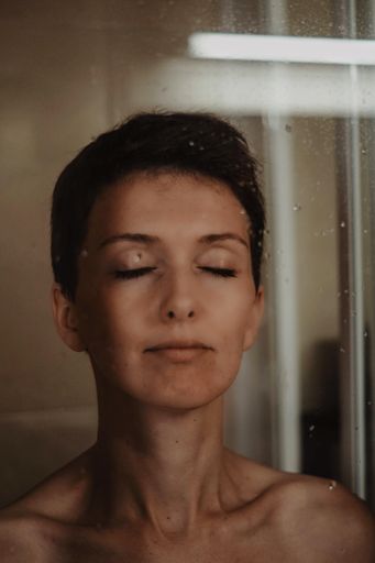 A beautiful middle-aged female on the other side of the glass wall splashed with water drops