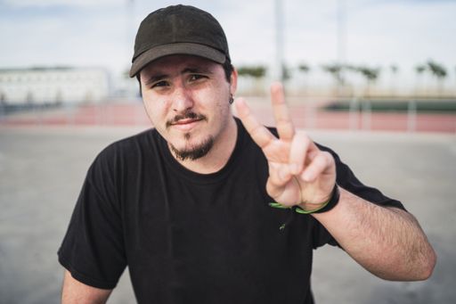 A selective focus shot of a smiling man in a black cap doing a peace sign with a blurred background