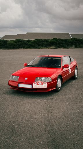 A red Alpine V6 turbo in a parking lot under the cloudy sky