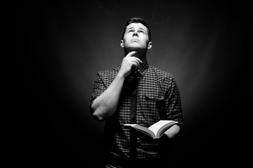 A black and white image of a man looking up with a book in his hands, appearing to be in thought.
