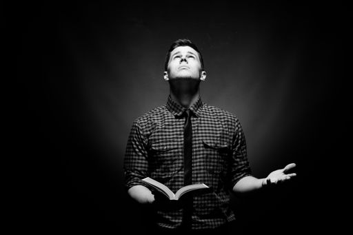 A black and white image of a man looking up with a book in one hand and a questioning expression.