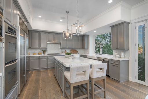 A modern kitchen with marble countertops, wooden floors, light gray cabinets, and an island