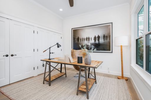 A stylish home office with white closets, large windows, and a rug
