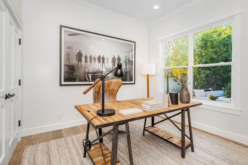 A stylish home office with white closets, large windows, and a rug