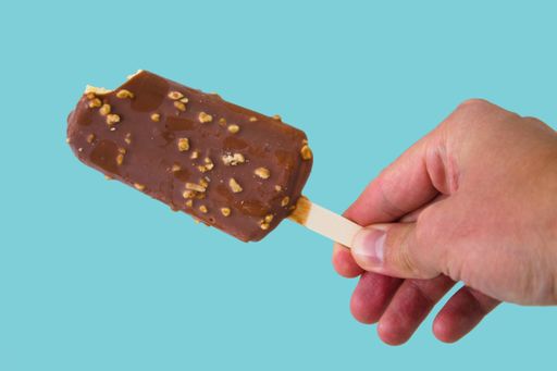 A closeup of a person holding an ice cream bar with nuts against a blue background