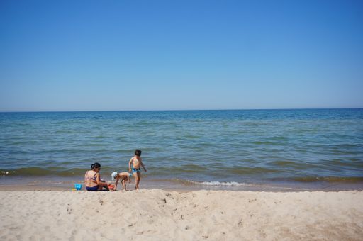 Woman and two kids close by the water and sand at a sandy beach.
